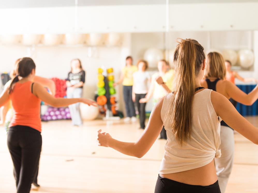 Gruppe von Frauen in Sportkleidung beim Tanztraining in einem gut beleuchteten Fitnessraum mit Spiegeln.